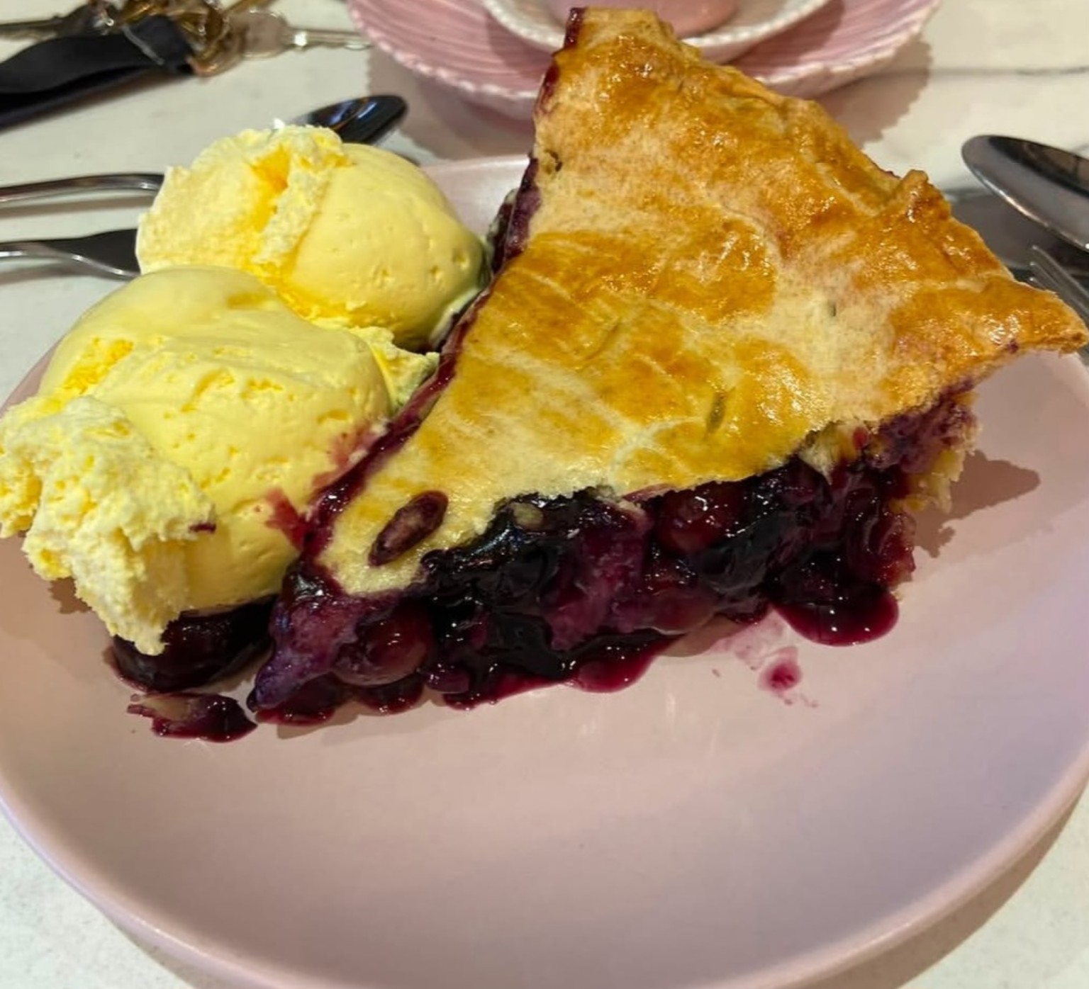 A generous slice of berry pie served with two scoops of vanilla ice cream